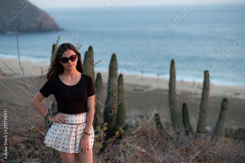 girl standing in the sunset with a beach and cactus on the background