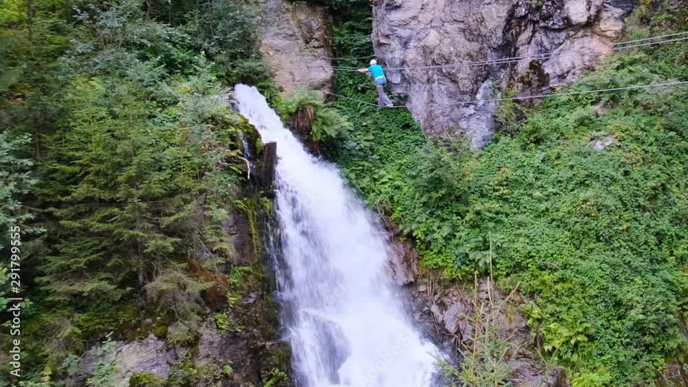 Male tourist crossing a via ferrata bridge towards the very tall Talbach waterfall in Austria, Zillertal area. Male tourist crossing a via ferrata bridge towards the very tall Talbach waterfall in Austria, Zillertal area.