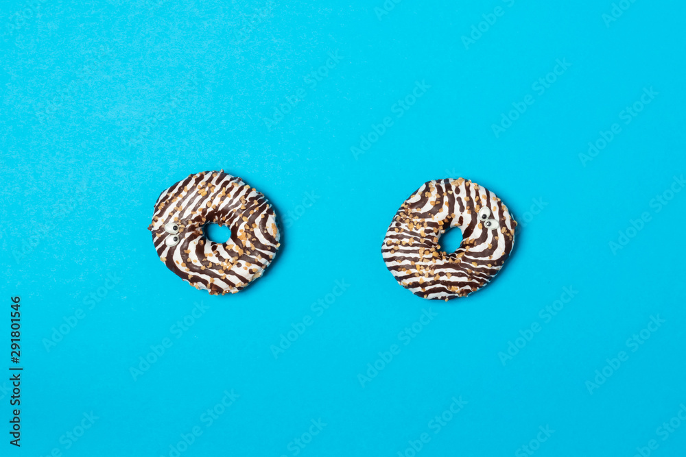 Naklejka premium Two white donuts with eyes and chocolate decoration with nuts against blue background. View from above.
