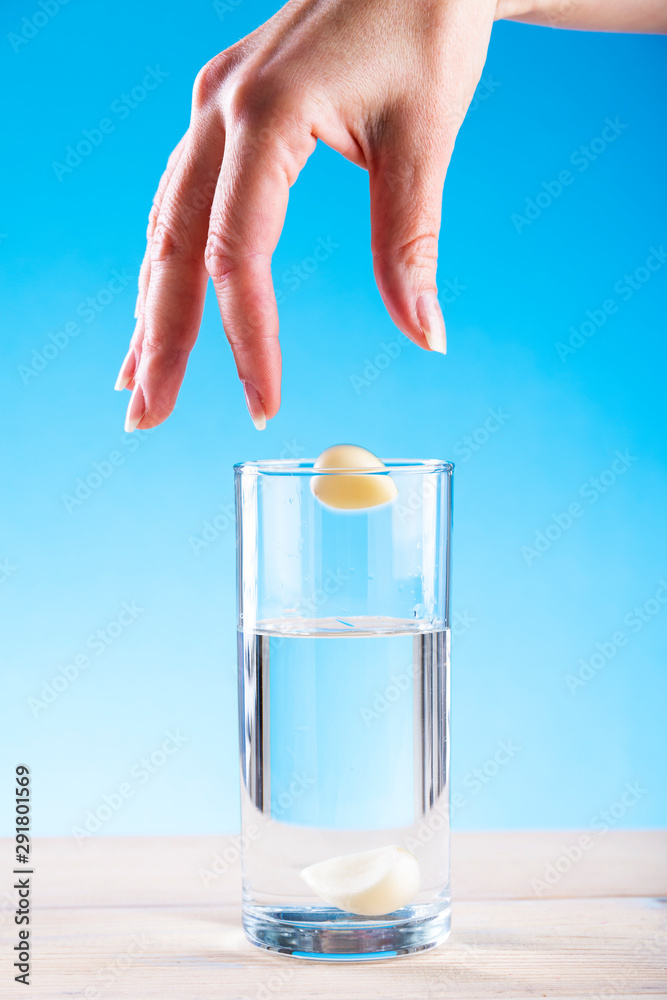 Hand throws garlic in a glass with water on a blue background, garlic water, disease prevention Hand throws garlic in a glass with water on a blue background, garlic water, disease prevention