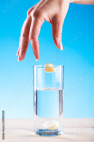 Hand throws garlic in a glass with water on a blue background, garlic water, disease prevention