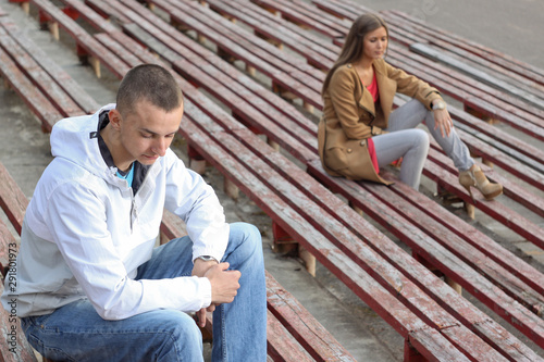 Sad boy and a girl sitting on tribunes of empty stadium.