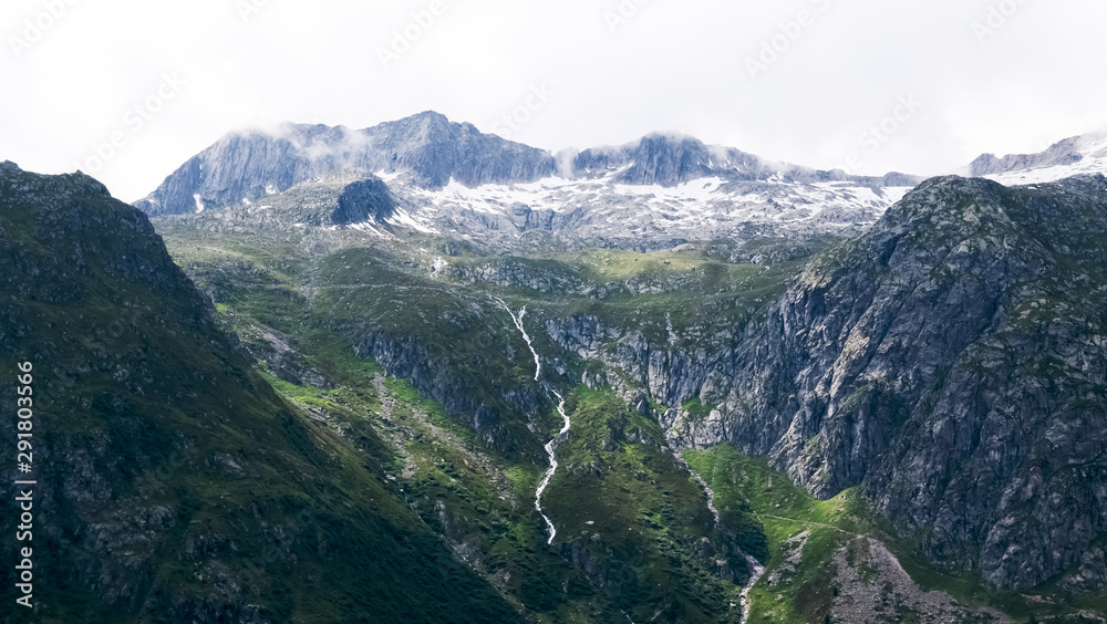 Stunning mountain in the alps seen closely with rocks, green pastures and stream