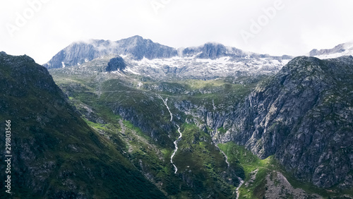 Stunning mountain in the alps seen closely with rocks, green pastures and stream