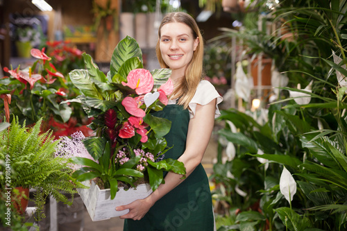 Сheerful woman florist holding pot with a flower in the gardening market © JackF