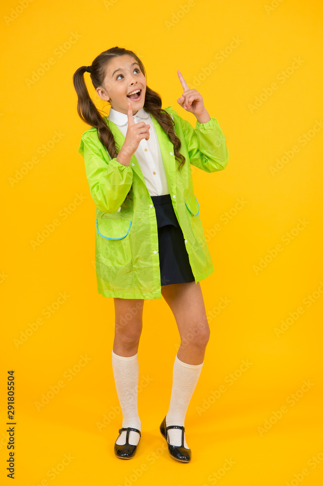 Look at the sky. Little schoolchild pointing finger up on yellow background. Little child wearing fashion rain jacket. Cute little kid enjoying rainy day activities. Happy little girl back to school