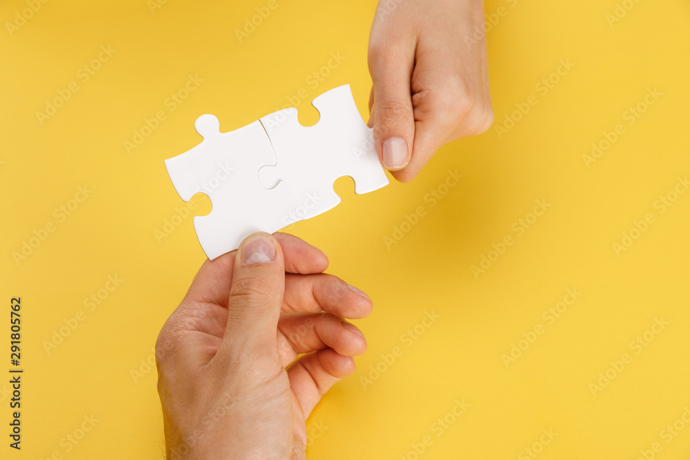 cropped view of man and woman holding pieces of white puzzle on yellow background - obrazy, fototapety, plakaty 