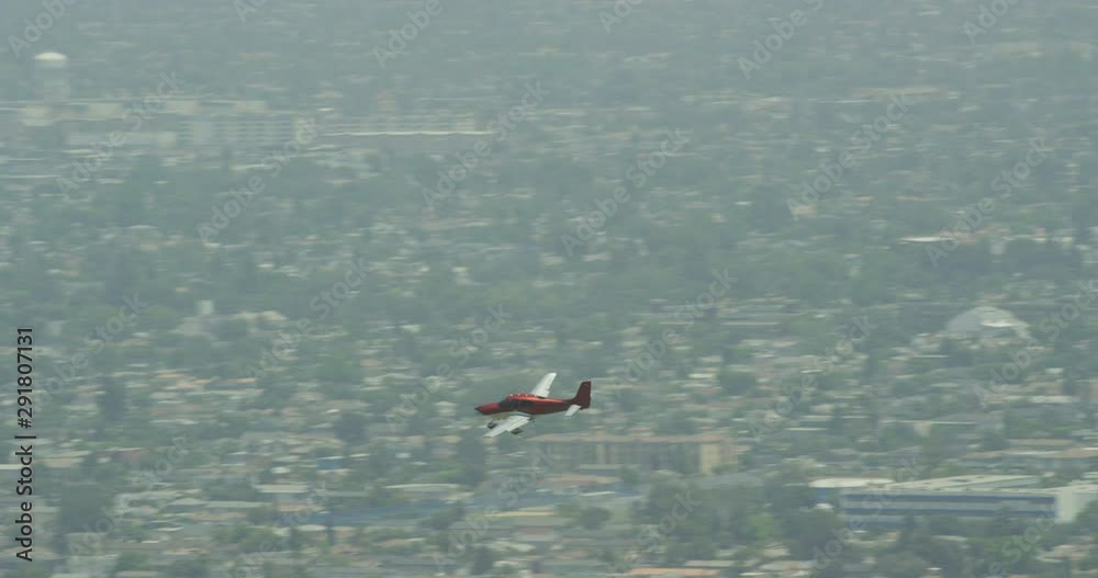 Small red plane flying over suburbs, overcast day, helicopter aerial, drone footage