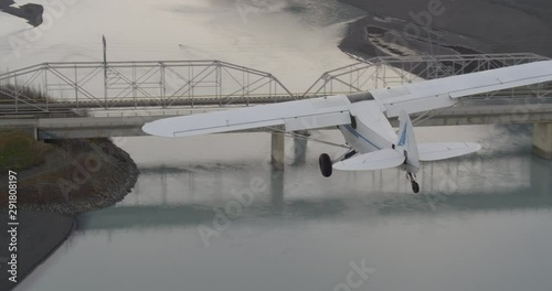 Helicopter aerial shot of biplane flying over bridge then descending over dry river, drone