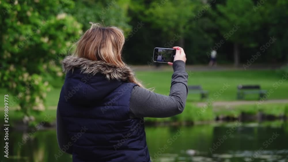 Girl stands with her back and takes a photo on her cell phone in Amsterdam park. Slow motion Girl stands with her back and takes a photo on her cell phone in Amsterdam park. Slow motion