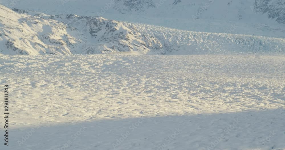 Aerial helicopter shot, track across details of rippling glacier at golden hour, zoom out to reveal mountains, drone footage Aerial helicopter shot, track across details of rippling glacier at golden hour, zoom out to reveal mountains, drone footage