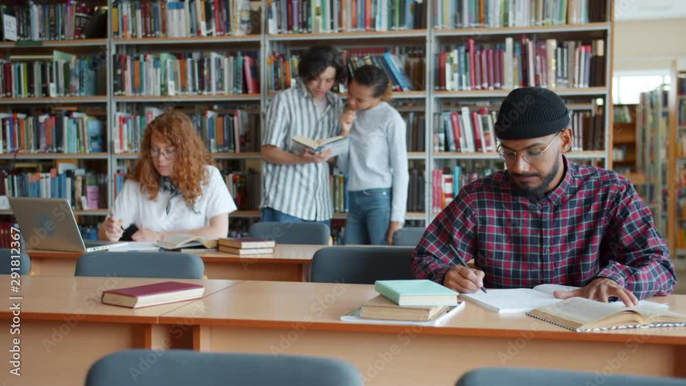 University students men and women are working in library reading books using laptop chatting enjoying education. People, culture and lifestyle concept.