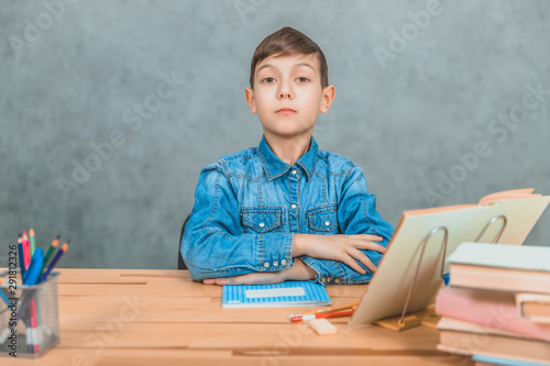 Smart serious schoolboy sitting with confident face expression  his hands folded on the desk.