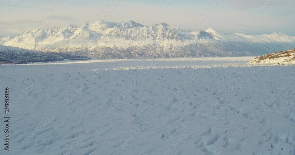 Aerial helicopter shot, push across rippling glacier at golden hour towards tall snowy mountains, tilt down towards glacial details drone footage Aerial helicopter shot, push across rippling glacier at golden hour towards tall snowy mountains, tilt down towards glacial details drone footage