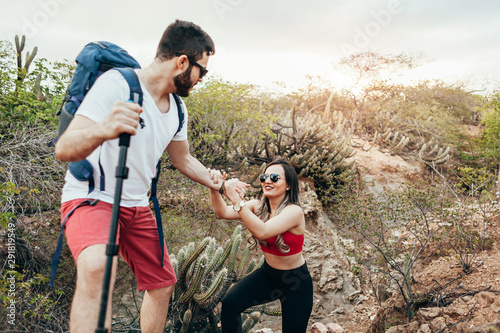Male hiker helping his girlfriend uphill in the countryside. Young couple hiking in desert