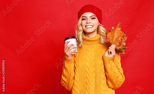 happy emotional cheerful girl laughing  with knitted autumn cap and Cup of coffee on colored red background.