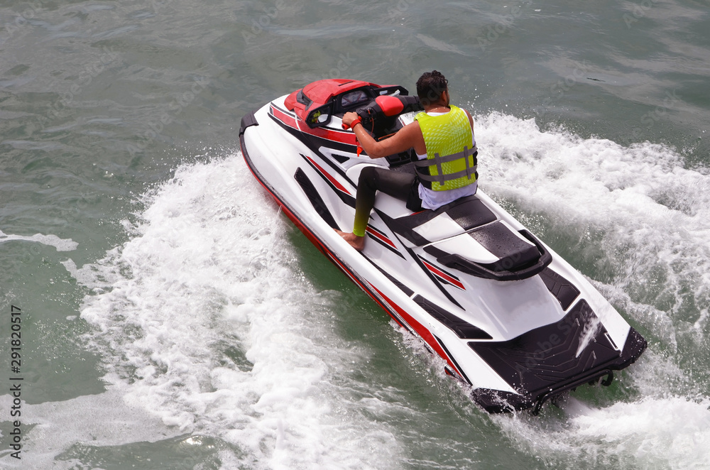 Fototapeta premium Angled overhead view of a man riding a speeding red and white jetski