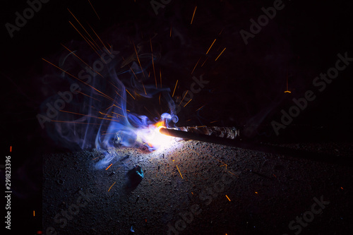 Arc welding. Welding of two sheets of metal by electrode in inert gases. Type MMA. A bright flash of light and a sheaf of sparks in a cloud of smoke. Miniature Universe. Free space for inscriptions.