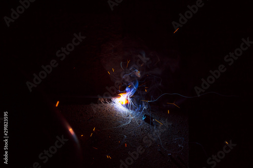 Arc welding. Welding of two sheets of metal by electrode in inert gases. Type MMA. A bright flash of light and a sheaf of sparks in a cloud of smoke. Miniature Universe. Free space for inscriptions.