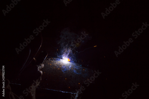 Fototapeta Naklejka Na Ścianę i Meble -  Arc welding. Welding of two sheets of metal by electrode in inert gases. Type MMA. A bright flash of light and a sheaf of sparks in a cloud of smoke. Miniature Universe. Free space for inscriptions.