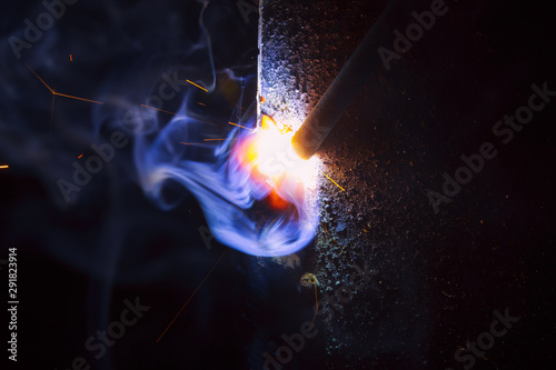 Arc welding. Welding of two sheets of metal by electrode in inert gases. Type MMA. A bright flash of light and a sheaf of sparks in a cloud of smoke. Miniature Universe. Free space for inscriptions.