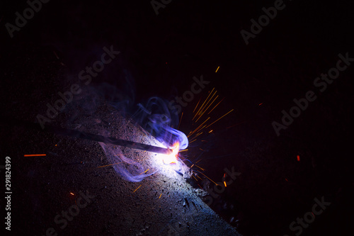 Arc welding. Welding of two sheets of metal by electrode in inert gases. Type MMA. A bright flash of light and a sheaf of sparks in a cloud of smoke. Miniature Universe. Free space for inscriptions.