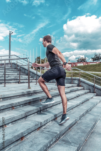 Fototapeta Naklejka Na Ścianę i Meble -  Athlete male athlete running in the summer in the city on a morning run on the stairs, view from the back from the side, sportswear, motivation lifestyle active.