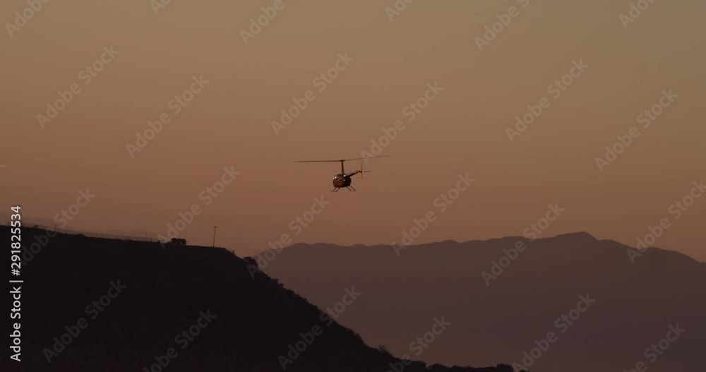 Aerial shot, day, distant view of back of helicopter approaching hollywood sign at sunset, drone
