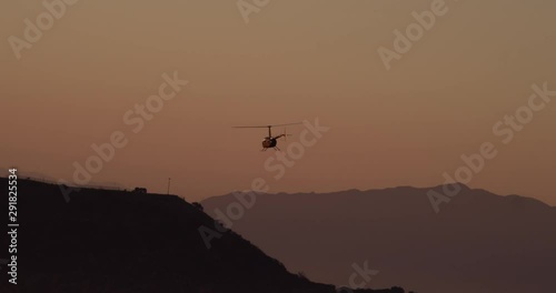 Aerial shot, day, distant view of back of helicopter approaching hollywood sign at sunset, drone