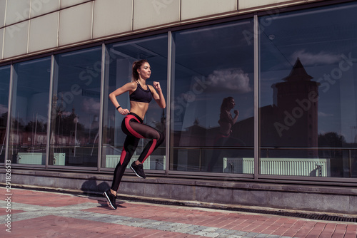 Beautiful athletic tanned athlete girl run summer city background glass windows  free space for fitness motivation text. Sportswear. Leggings. Top. Sneakers. Stylish fashionable slender woman.