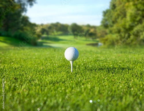 Low angle view of golf ball on a tee in front of a sunny fairway