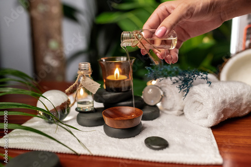 A girl pours oil from a jar of aromatic oils standing on stones for stone therapy and located on a terry towel next to which are transparent spheres, a twisted towel and a sprig of lavender