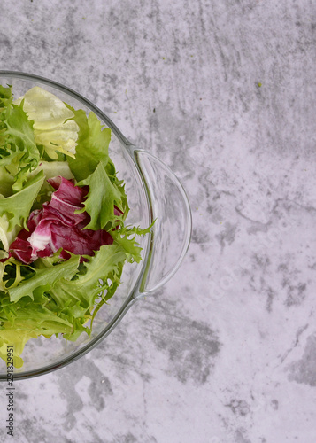 Salad. Organic food. Healthy vegetable salad with escarole endive, frisee endive, chicory radicchio, lettuce in a glass bowl. Gray table top background. Top view. Vegetarian food.
