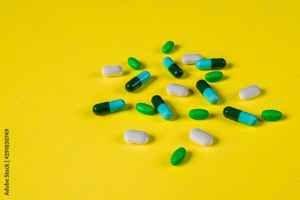 Capsules with a medicine of white and blue-green color scattered in the right corner on a yellow background.The concept of pharmacology.