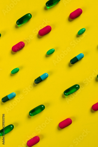 Tablets and pills of various shapes and colors laid out on a yellow background. Medicine concept.