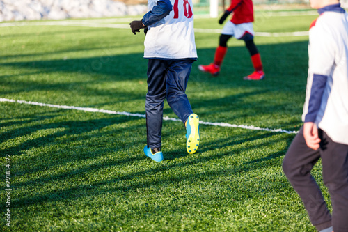 Boys in white and red sportswear plays football on field, dribbles ball. Young soccer players with ball on green grass. Training, football, active lifestyle for kids , winter sport