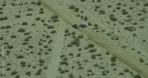 Helicopter aerial shot of dune buggies riding through desert path, drone