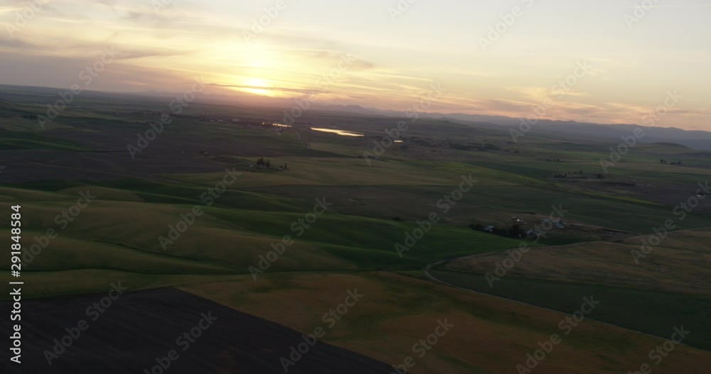 Tilted helicopter aerial shot of sun setting beyond green fields, drone Tilted helicopter aerial shot of sun setting beyond green fields, drone