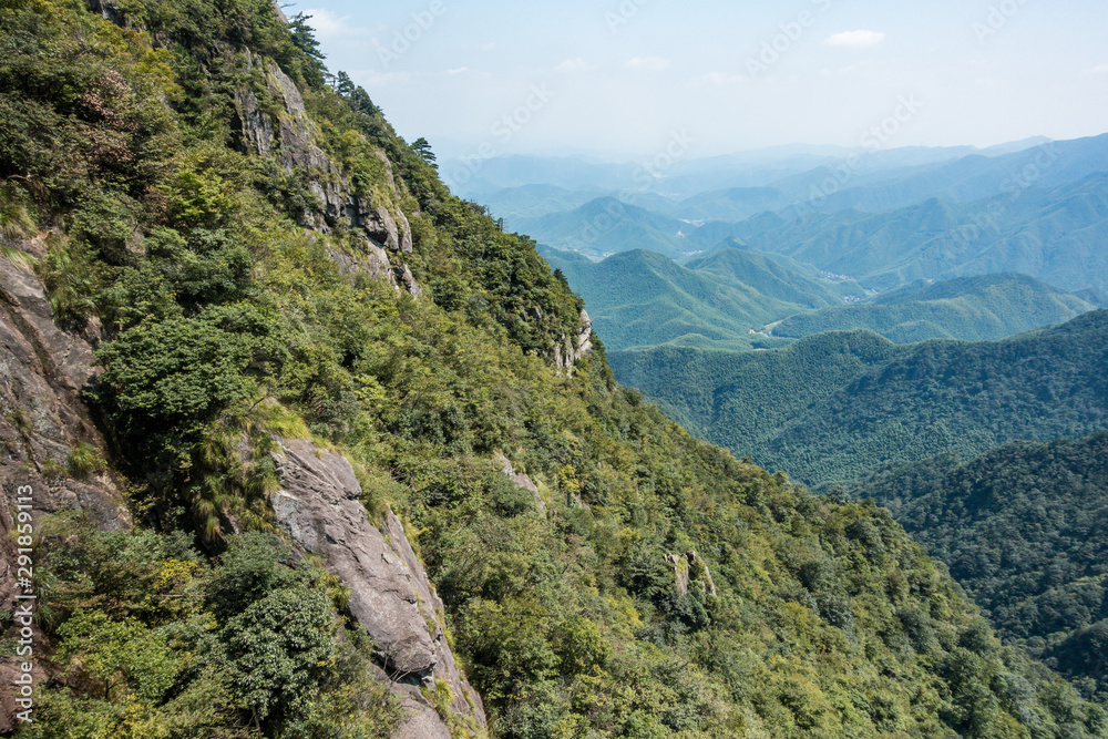 slope on the mountain covered with green forest with forest covered valley in the background on a hazy day