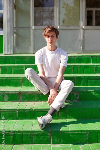 Portrait of a young guy of model appearance sitting on the green steps