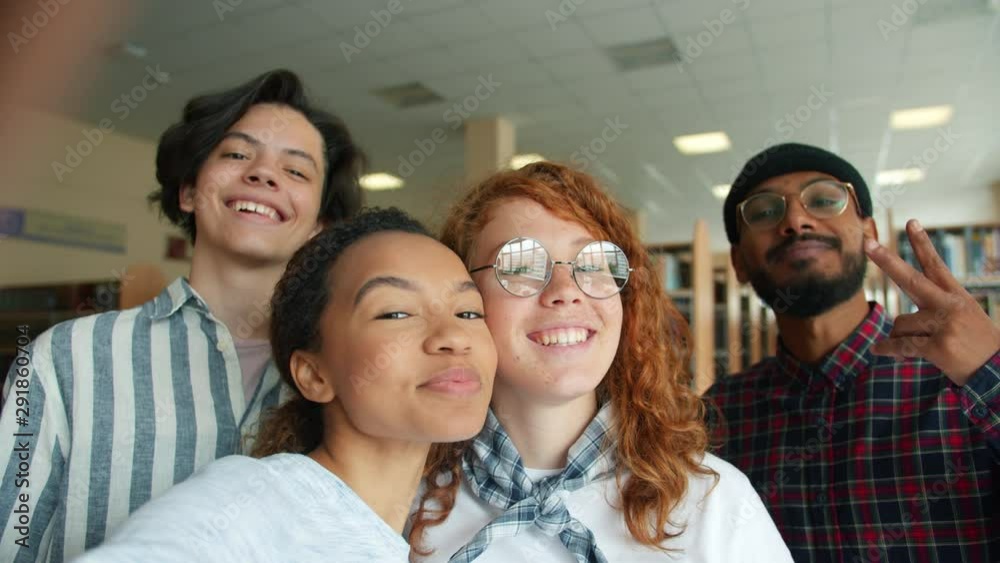 Multi-ethnic group of students girls and guys are taking selfie posing looking at camera smiling standing in library together. Lifestyle and photograph concept. Multi-ethnic group of students girls and guys are taking selfie posing looking at camera smiling standing in library together. Lifestyle and photograph concept.