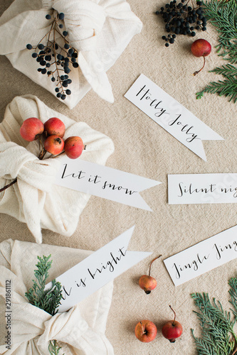 CHristmas greetings handwritten on tags close to gifts wrapped inside cotton napkins and decorated with botanical elements photo