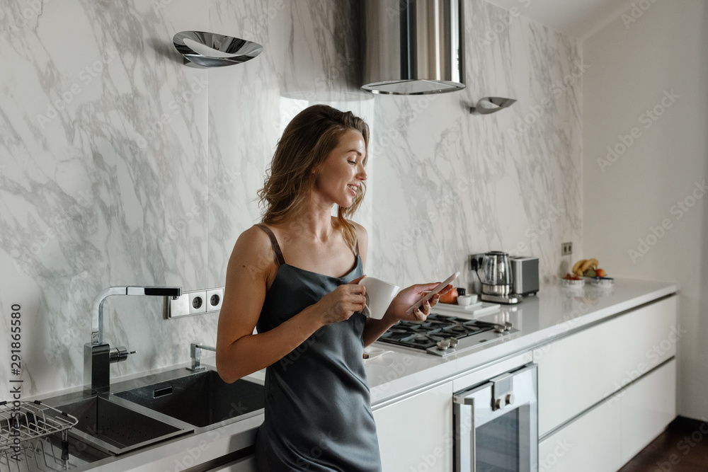 Woman with coffee using phone in kitchen Woman with coffee using phone in kitchen