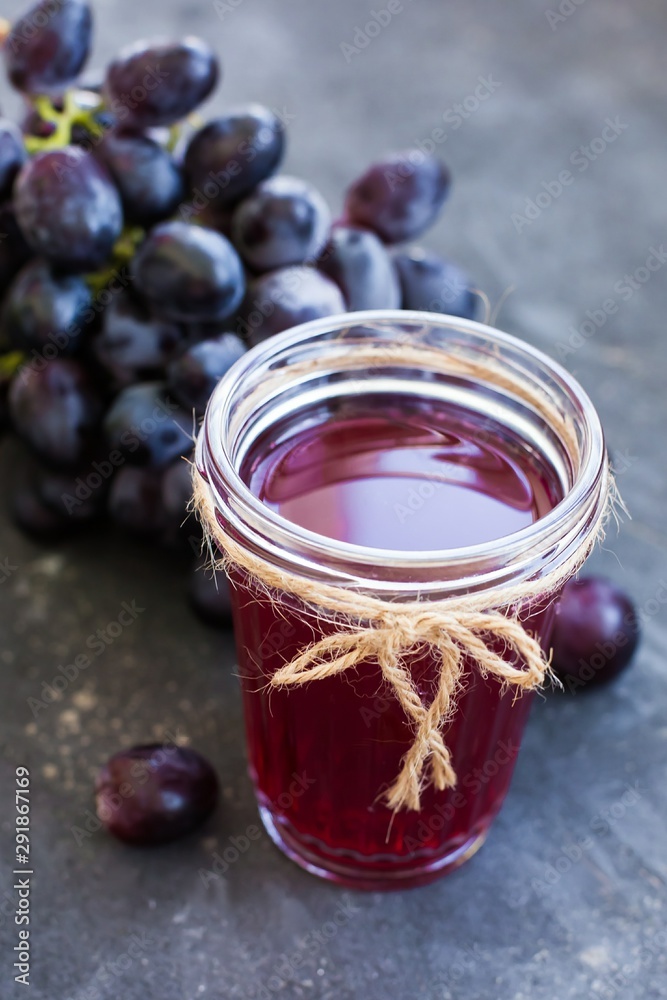A bunch of ripe blue grapes and a glass of grape juice close-up on a blue shabby concrete background. A bunch of ripe blue grapes and a glass of grape juice close-up on a blue shabby concrete background.