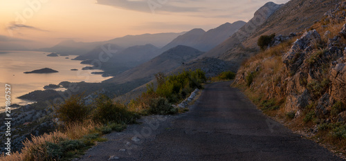 a narrow, winding road that runs on the edge of a cliff above Lake Skadar in Montenegro