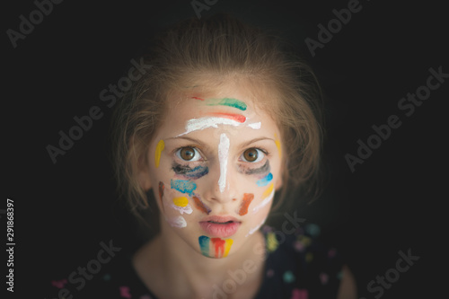 beautiful portrait of little caucasian kid girl face with big eyes with colorful art painting on her with multicolor paint