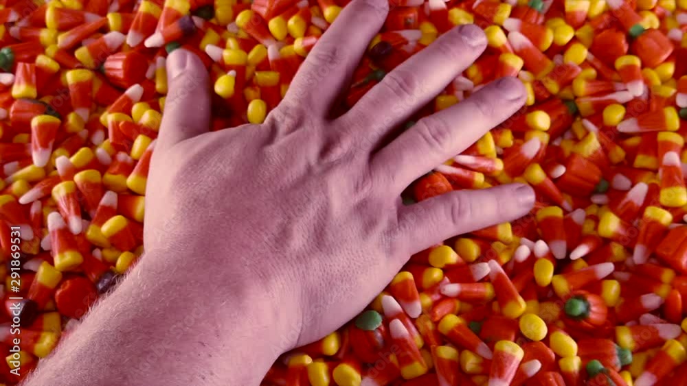 A hand is seen grabbing into a large pile of Halloween candy corn and pumpkins.