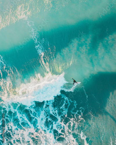 Canvas Print Aerial sport action shot of a surfer at sunrise riding a wave in a blue ocean in