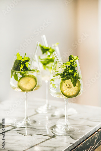 Hugo Sparkling wine cocktail with fresh mint and lime in glasses with eco-friendly straws over white marble kitchen counter, selective focus. Cold refreshing summer alcoholic drink