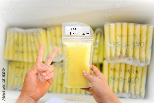 Hands holding Breast Milk Storage Bag in front of stocks in freezer refrigerator photo